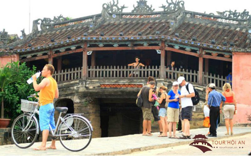 (Los turistas andan en bicicleta para explorar el puente cubierto japonés en Hoi An)